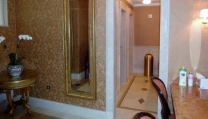 Talisen Construction Corporation: Construction Management and General Contractor. University Club, 1 West 54th Street, New York. Ornate bathroom with custom stonework floors and intricate wallpaper with laurel design. gold garbage container is at the end of the hallway. A golden-trim mirror hangs on the wall.