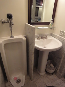 Talisen Construction Corporation: Construction Management and General Contractor. University Club, 1 West 54th Street, New York. A urinal and sink separated by a marble partition. A mirror hangs above the sink