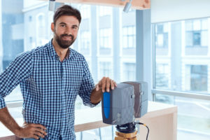 smiling man on job site stands beside 3D laser scanner