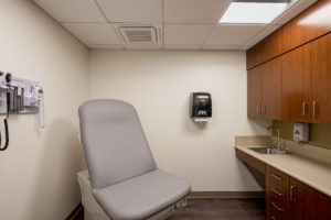 exam room with chair, medical equipment, hand wash station, and cabinets
